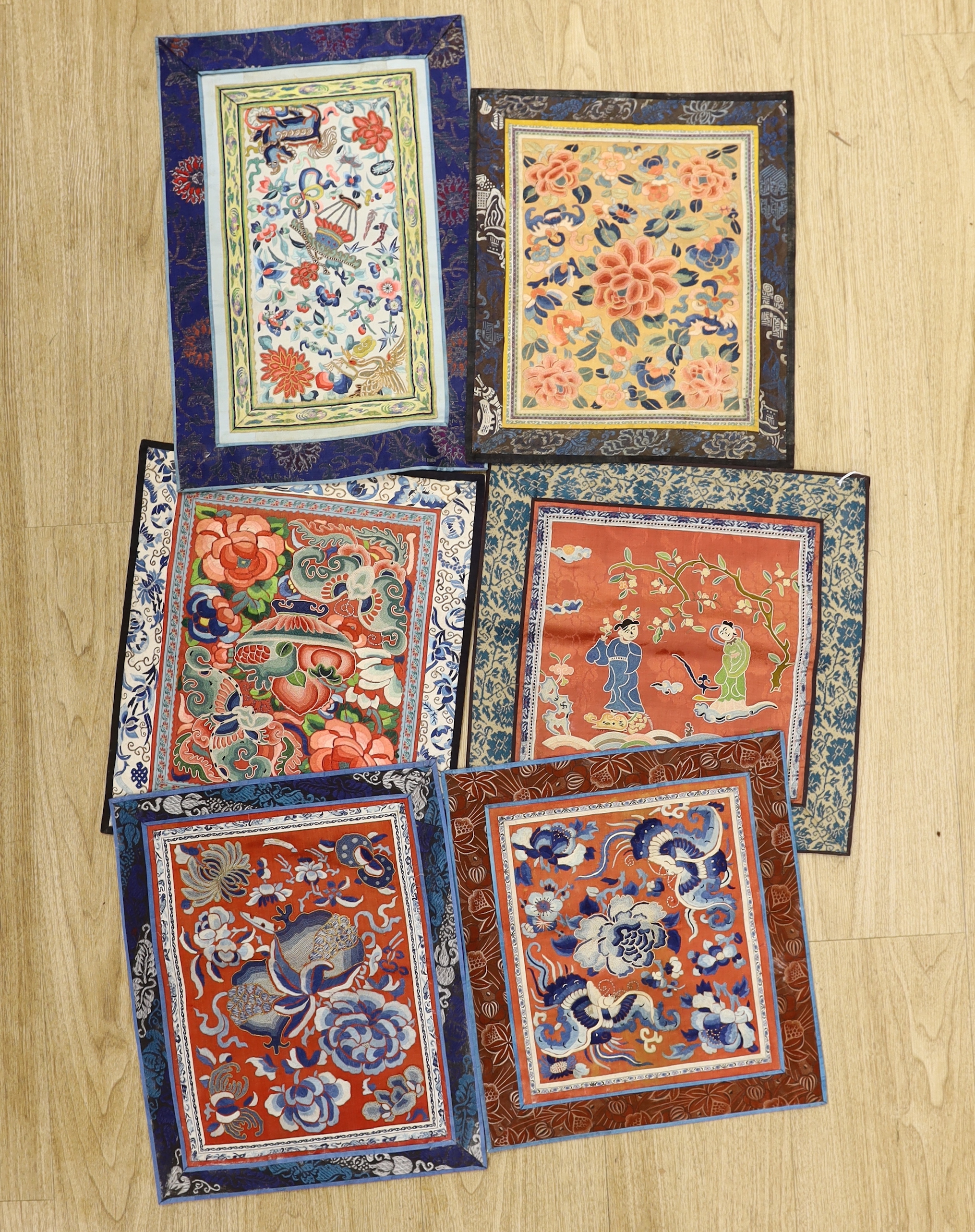 Six Chinese silk embroidered panels, embroidered with Beijing knot and stem stitch, using auspicious symbols: figures, flowers, butterflies and one with a dragon, five bordered with silk brocade, largest 48cm high x 32cm